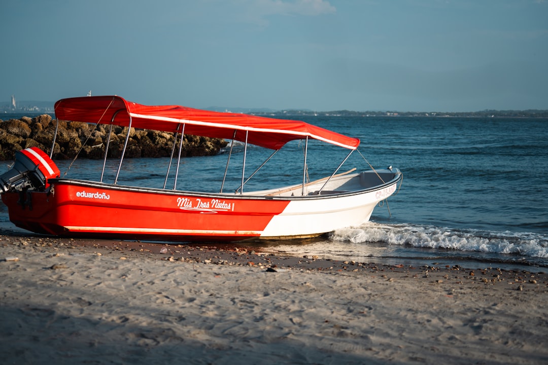 Barque rouge et blanche sur la plage de Carthagène, Colombie, avec les eaux turquoise de la mer des Caraïbes en arrière-plan